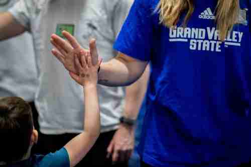 A small child high fives a GVSU student wearing a blue shirt reading 'Grand Valley State'